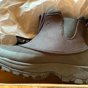 Svarta vattentäta chelsea boots med dubbar - Svarta vinterskor med grov sula och dubbar för extra grepp. Skorna är vattentäta och har elastiska partier på sidorna för enkel påtagning. Perfekta för blöta och hala dagar. Ovandelen är i syntetmaterial och sulan är robust och slitstark. Ordinarie pris 999kr. Säljes pga felköp, finns även stl 38