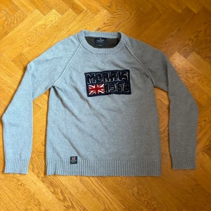 Grå bomullströja Morris  - Snygg grå tröja från Morris i 100% bomull med broderad patch framtill där det står 'Morris 1968' och en brittisk flagga. Tröjan har rund halsringning, långa ärmar och ribbade muddar. Perfekt för dig som gillar klassisk stil med en twist.