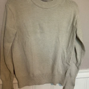 Beige stickad tröja från H&M - En stilren beige stickad tröja från H&M i storlek S. Tröjan har rund halsringning, ribbade muddar och är långärmad. Perfekt för lager-på-lager och enkel att matcha med jeans eller kjol.