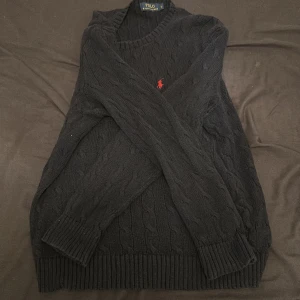 Svart kabelstickad tröja Polo Ralph Lauren - Kabelstickad svart tröja från Polo Ralph Lauren i storlek L. Klassisk design med rund hals, ribbade muddar och röd broderad logga på bröstet. Perfekt för dig som gillar stilrena och tidlösa plagg med premiumkänsla. Vill ni prata om priset kan ni skriva till mig ,hälar Lidingö 😃 den är ganska ny