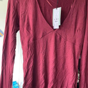 Vinröd v-ringad topp från Gina Tricot - Superskön vinröd långärmad topp från Gina Tricot med djup v-ringning. Modellen är figurnära och i mjuk bomullsmix, perfekt för dig som gillar en enkel men snygg look. Färgen heter zinfandel och ger en riktigt trendig vibe.