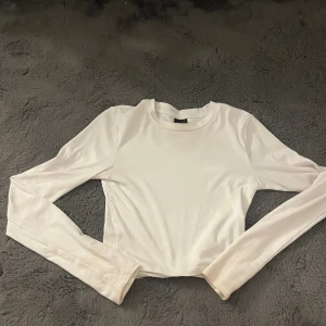 Vit croppad långärmad topp - En stilren vit croppad topp med långa ärmar och rund hals. Perfekt att matcha med höga jeans eller kjol för en clean look. Mjuk och stretchig känsla, enkel att styla till olika outfits.