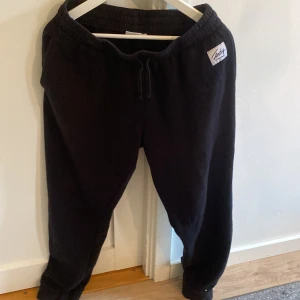 Svarta mjukisbyxor Andy XL - Svarta mjukisbyxor från Andy by Frank Dandy i storlek XL. De har resår i midjan med snörning och en enkel, avslappnad passform. Perfekta för chill dagar eller när du vill vara extra bekväm. Klassisk look utan onödiga detaljer.