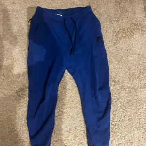 Blå Nike mjukisbyxor (finns överdel i profilen) - Snygga blå mjukisbyxor från Nike med svart logga på låret. Byxorna har dragsko i midjan och två sidofickor. Perfekta för chill eller träning, med en skön passform och mjukt material.