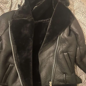 Svart pälsjacka från NA-KD, stl 36 - Säljer en svart pälsjacka från NA-KD i storlek 36. Jackan har en cool oversized krage, mjuk fuskpäls på insidan och grova dragkedjor. Utsidan är i skinnimitation med en schysst struktur. Perfekt för dig som vill ha en statementjacka till vintern.