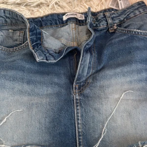 Blå jeans från Pull&Bear, storlek 36 - Säljer ett par klassiska blå jeans från Pull&Bear i storlek 36. Jeansen har fem fickor, dragkedja och knapp framtill samt snygga slitningar och ljusare tvätt på låren. Perfekta för en avslappnad och trendig look. Köpte dem förra året i Portugal men har inte använt dem sen 