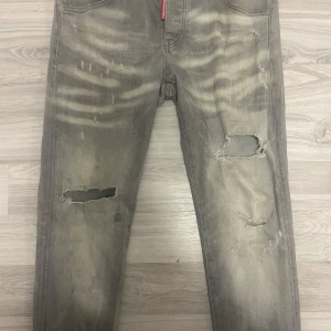Grå slitna jeans från Dsquared2 - Fickorna är sönder men priset är inte hugget i sten Riktigt snygga grå jeans från Dsquared2 med coola slitningar och hål på benen. Jeansen har en tvättad look med ljusa partier och klassiska fem fickor. Perfekta för dig som gillar en edgy streetstil.