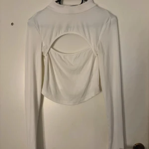 Vit ribbad långärmad polotopp - Trendig vit ribbad polotopp med lång ärm och cool öppen ryggdetalj. Toppen är croppad och har en snygg, figurnära passform som passar perfekt till jeans eller kjol. Materialet är mjukt och stretchigt för extra komfort. Obs. Sminkfäck, går säkert bort med galltvål‼️