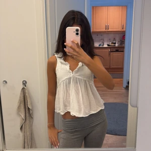 Vit volangblus med v-ringning från Gina Tricot💕 - Supersöt vit blus med volangdetaljer och v-ringning. Den är ärmlös och har en luftig, flowy passform som ger en romantisk vibe. Perfekt till jeans eller kjol för en fräsch look. Gjord i tunn bomull som känns lätt och sval. Från Gina tricot i storlek 146/152, ställ frågor!!💕