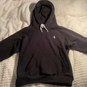 Svart hoodie från Polo Ralph Lauren - Svart hoodie från Polo Ralph Lauren med vit broderad logga på bröstet och vit snörning i huvan. Tröjan är helt oanvänd men prislappen är tyvärr borta. Skriv gärna vid frågor. Nypris 2195. Pris kan diskuteras💕