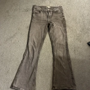 Grå bootcut jeans från Gina Tricot - Snygga grå jeans från Gina Tricot i storlek 158. Modellen har bootcut-ben, klassiska fem fickor och dragkedja med knapp framtill. Jeansen har en tvättad look och är tillverkade i ett mjukt bomullsmaterial med lite stretch.