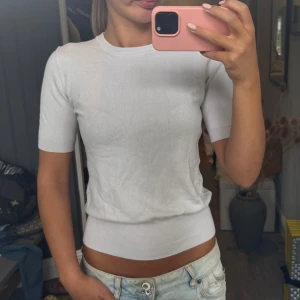 Vit stickad t-shirt från zara - En stilren vit topp med rund hals och korta ärmar. Toppen har ribbade muddar vid ärmslut och midja för en snygg passform. 