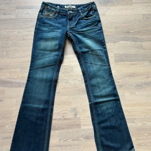 Blå lågmidjade bootcut jeans - Säljer ett par unika sjukt snygga blå lågmidjade bootcut jeans med broderade detaljer på bakfickorna. Jeansen är i storlek 27💗