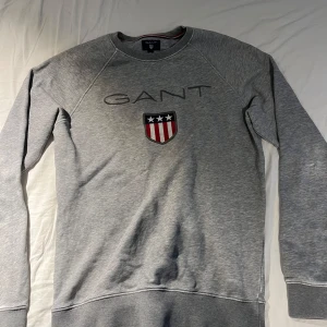 Grå sweatshirt från GANT med logga - Säljer en grå sweatshirt från GANT i storlek XS. Tröjan har GANT-logga och ett broderat sköldmärke framtill. Klassisk rund halsringning och långa ärmar. Perfekt för en chill och stilren look. Har använt några gånger. Kontakta om frågor, priset är inte ristat i sten.