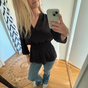 Svart blus med v-ringning och resår  - Säljer en svart blus med v-ringad hals och trekvartsärmar. Blusen har en resår midja. Köpt second hand och har bortklippt lapp, därför inget märke. 