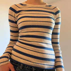 Randig ribbad tröja från H&M - Säljer en ribbad långärmad tröja från H&M i storlek XS. Tröjan är vit / beige med blå ränder, har en tight passform och rund halsringning. Perfekt för lager-på-lager och funkar året runt. Superstretchigt och mjukt material.
