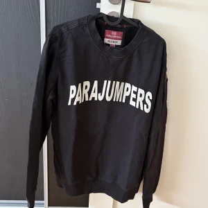 Svart sweatshirt från Parajumpers - Svart sweatshirt från Parajumpers med stor vit logga framtill. Klassisk rund halsringning och långa ärmar. Tillverkad i mjuk bomullsfleece som är skön mot huden. Perfekt för en avslappnad och stilren look.