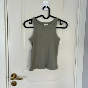 Ribbad grå linnetopp från Kappahl - Snygg ribbad grå linnetopp från Kappahl med klassisk rund halsringning och ärmlös design. Perfekt för varma dagar eller som lager under skjortor och jackor. Enkel och stilren modell som passar till det mesta.