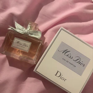 Miss Dior Eau de Parfum 100ml - Miss Dior Eau de Parfum från Dior i en elegant glasflaska med ljusrosa doft och en söt, glittrig rosett vid halsen. Flaskan rymmer 100 ml och kommer med originalkartong. Perfekt för dig som älskar lyxiga och feminina parfymer.