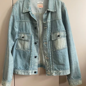 Ljusblå jeansjacka från Gant - Säljer en klassisk ljusblå jeansjacka från Gant i 100% bomull. Jackan har två bröstfickor med knappar, slitna detaljer och svarta knappar framtill. Perfekt oversized vibe och passar till allt. Snygga sömmar och tidlös design.