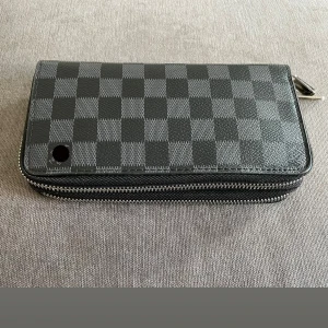 Plånbok - Snygg plånbok i klassisk Damier Graphite-mönster helt ny oanvänd. Svart och grå ruta i tåligt skinn med dubbla dragkedjor och flera fack för kort och kontanter. Perfekt accessoar för dig som gillar stilren och lyxig design, pris kan diskuteras vid snabb affär.