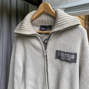 Beige stickad kofta från G-Star RAW - Säljer en beige stickad kofta från G-Star RAW med hög krage och hel dragkedja. Väldigt tung bomull - bra kvalitet- köpt i Barcelona för 22 euro 