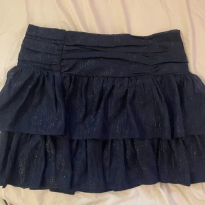 Marinblå glittrig volangkjol - Supersöt marinblå minikjol med volanger och glittrigt tyg. Den är från Gina Tricot Young och i storlek 158/164 men skulle säga att den är som en XS. Den är helt ny och har prislappen kvar. Helt slutsåld och säljs inte längre, därav priset. Säljer då den tyvärr inte passar. Det är bara att höra av sig vid frågor och skriv helst innan köp! 🪽💗