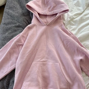 Ljusrosa hoodie  - Säljer en ljusrosa hoodie med stor huva och magficka. Tröjan har en relaxed passform och är tillverkad i mjuk bomullsmix, perfekt för chill dagar. Långa ärmar och ribbade muddar vid ärmslut och nederkant. Enkel och stilren design utan tryck.