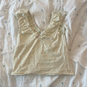 Ljusgul linnetopp från Urban Outfitters - Supersöt beige linnetopp från Urban Outfitters med volangkantade axelband och v-ringning. Toppen har en liten rosett framtill och är ärmlös med en feminin, romantisk vibe. Perfekt att styla med jeans eller kjol för en chill look. Skriv gärna om du undrar något!!💕💕