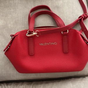 Röd Vintage  handväska från Valentino - LIMITED EDITION handväska från Valentino med guldfärgade detaljer och dragkedja. Väskan är i präglat skinn och har både handtag och axelrem. En väska som verkligen står ut i mängden!! Har fått många komplimanger med den. OBS. SÄLJS EJ LÄNGRE, därav priset