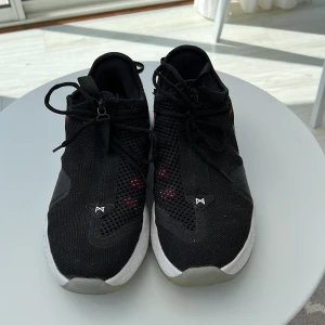 Svarta Nike PG 4 sneakers - Säljer ett par svarta Nike PG 4 sneakers med vit sula och silverfärgad swoosh. Ovandelen är i mesh med röda detaljer och snörning. Skorna har rund tå och platt sula, samt diskreta signaturdetaljer på hälen. Perfekta för dig som gillar sportig och clean stil.