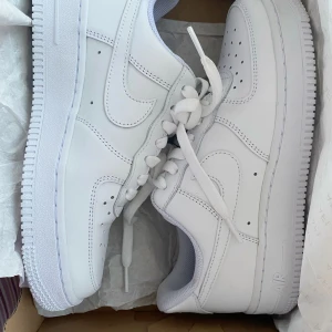 Nike Air Force 1 helvita sneakers - Använt endast en gång. Klassiska Nike Air Force 1 i helvitt skinn med vit sula och snörning. Snygg och tidlös modell med perforerade detaljer på tån och ikonisk swoosh på sidorna. Perfekta för dig som vill ha en clean och fräsch look till vardags.