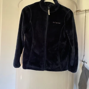 Svart fleecejacka från On The Peak - Mysig svart fleecejacka från On The Peak med hel dragkedja framtill och hög krage. Jackan har en enkel och stilren design, och är väldigt varm och skön.