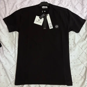 Stone Island T-shirt - Svart t-shirt från Stone Island med klassisk rund hals och ikonisk logopatch på bröstet. Tillverkad i 100% bomull för en skön och clean känsla. Perfekt basic med snygg passform och diskret branding. Enkelt att matcha till allt.