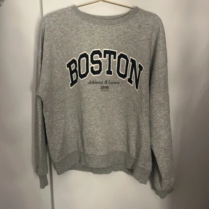 Grå sweatshirt  - Grå sweatshirt från H&M i storlek XS med svart och vit BOSTON-tryck framtill. Klassisk rund halsringning, ribbade muddar vid ärmslut och nederkant. Perfekt för en chill och sportig look. Inte använd särskilt mycket
