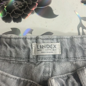 Grå jeansbyxor från Lindex Betty - Snygga grå jeansbyxor från Lindex Betty med klassisk femficksmodell och bälteshällor. Byxorna har dragkedja och knapp framtill och är tillverkade i ett mjukt bomullstyg med jeansstruktur. Perfekta för en avslappnad och trendig look.