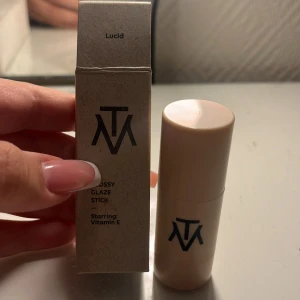 Glossy Glaze Stick Lucid från TM - Glossy Glaze Stick i nyansen Lucid från TM. En krämig highlighter-stick med glansig finish, berikad med vitamin E. Kommer i en beige plastförpackning med svart logga. Perfekt för att ge glow till kindben, näsrygg eller amorbåge. I fint skick! 