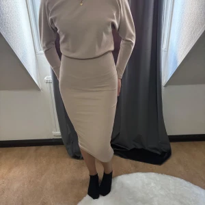 Beige ribbad långklänning - Snygg beige långklänning med ribbad struktur och lång ärm. Klänningen har en kroppsnära passform och är tillverkad i ett mjukt, stretchigt material som sitter skönt. Perfekt för dig som gillar en stilren och enkel look.