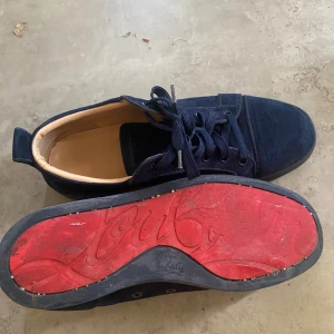 Mörkblå sneakers från Christian Louboutin - Äkta Christian Louboutin, endast använd några gånger. Har tyvärr inte boxen till skorna. Snygga mörkblå sneakers från Christian Louboutin i mocka med klassisk röd sula och rund tå. Skorna har svarta snören och en stilren design som sticker ut med den ikoniska röda undersidan. Perfekta för dig som vill ha något exklusivt och unikt.