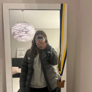 Mörkgrå pufferjacka från Nike  - Säljer en mörkgrå pufferjacka från Nike i storlek XL. Jackan har huva, dragkedja framtill och två fickor med knappar. Klassisk Nike-logga på bröstet och skön, vadderad känsla. Perfekt för kalla dagar och riktigt snygg streetstil. Har en liten skråma som syns på bild 5 men inget man ens tänker på. Sitter som en storlek M.