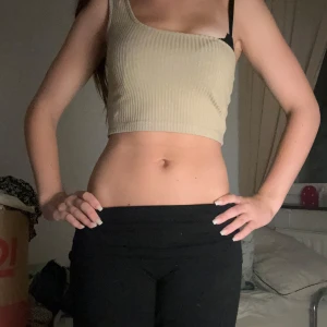 Beige ribbad croppad one shoulder topp - Säljer en beige croppad topp med ribbad struktur och asymmetrisk one shoulder-design. Toppen är ärmlös och har en snygg, modern passform som sitter tight. Perfekt för dig som gillar trendiga och stilrena plagg.