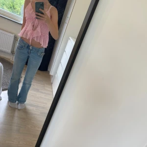 Rosa volangig linnetopp med knyt - Supersöt ljusrosa linnetopp med volanger och smala axelband. Toppen har ribbad struktur, knyt framtill och flera lager volangdetaljer som ger en romantisk vibe. Perfekt för varma dagar och somriga outfits! Pris kan diskuterats