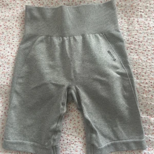 Grå träningstights-shorts Gymshark - Säljer ett par grå vinted shorts från Gymshark. De har bred ribbad midja, tight passform och är perfekta för gymmet eller annan träning. Materialet är stretchigt och mjukt, med diskret Gymshark-logga på sidan och stor logga på baksidan. Säljer då jag inte använder dem. Shortsen går inte längre att köpa på hemsidan💗💕