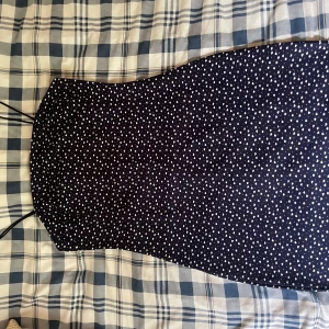 Marinblå klänning med vita hjärtan - Supersöt marinblå klänning med vita hjärtan och tunna axelband. Figurnära passform och kort längd, perfekt för varma dagar. Mönstret ger en lekfull vibe och den är lätt att matcha med sneakers eller sandaler.