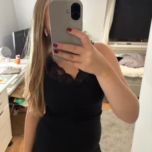 Svart spetslinnetopp - Säljer en svart ärmlös linnetopp med snygg spetsdetalj längs v-ringningen. Toppen har en tight passform och är perfekt att styla med jeans eller kjol. Superenkel men ändå elegant look!