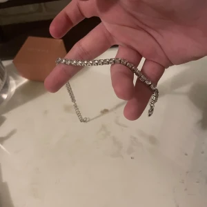 Silverfärgat armband med stenar - Snyggt armband i silverfärg med glittrande stenar längs hela bandet. Kedjan har en klassisk design och passar perfekt för dig som gillar stilrena smycken med lite extra bling.