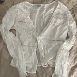 Vit blus med spetsdetaljer LCW Casual - Säljer en luftig vit blus från LCW Casual i storlek XS. Blusen har långa ärmar, v-ringning och knappar framtill. Snygga spetsdetaljer går tvärs över både fram- och baksidan. Perfekt för en fräsch och stilren look.