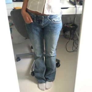 Lågmidjade Jeans - Säljer ett par blåa lågmidjade bootcut jeans från Brandy Melville. Skulle säga att det är storlek S. Köptes vintern 2022, men har de senaste två åren mest legat i garderoben. Defekt på sista bilden då bälteshällan är uttöjd.
