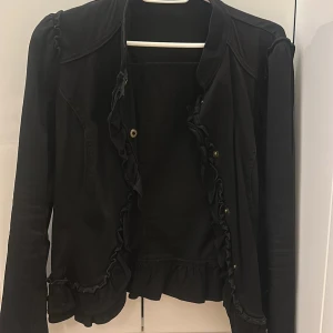 Svart volangjacka  - Svart jacka med volangdetaljer i jättefint skick. Kontakta för fler bilder, pris går att diskutera.