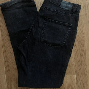 Svarta jeans från NLY Jeans - Snygga svarta jeans från NLY Jeans med klassisk femficksdesign och raka ben. Jeansen har en mörk tvätt och är tillverkade i ett robust jeanstyg med bälteshällor och knappstängning framtill. Perfekta för en stilren och avslappnad look.